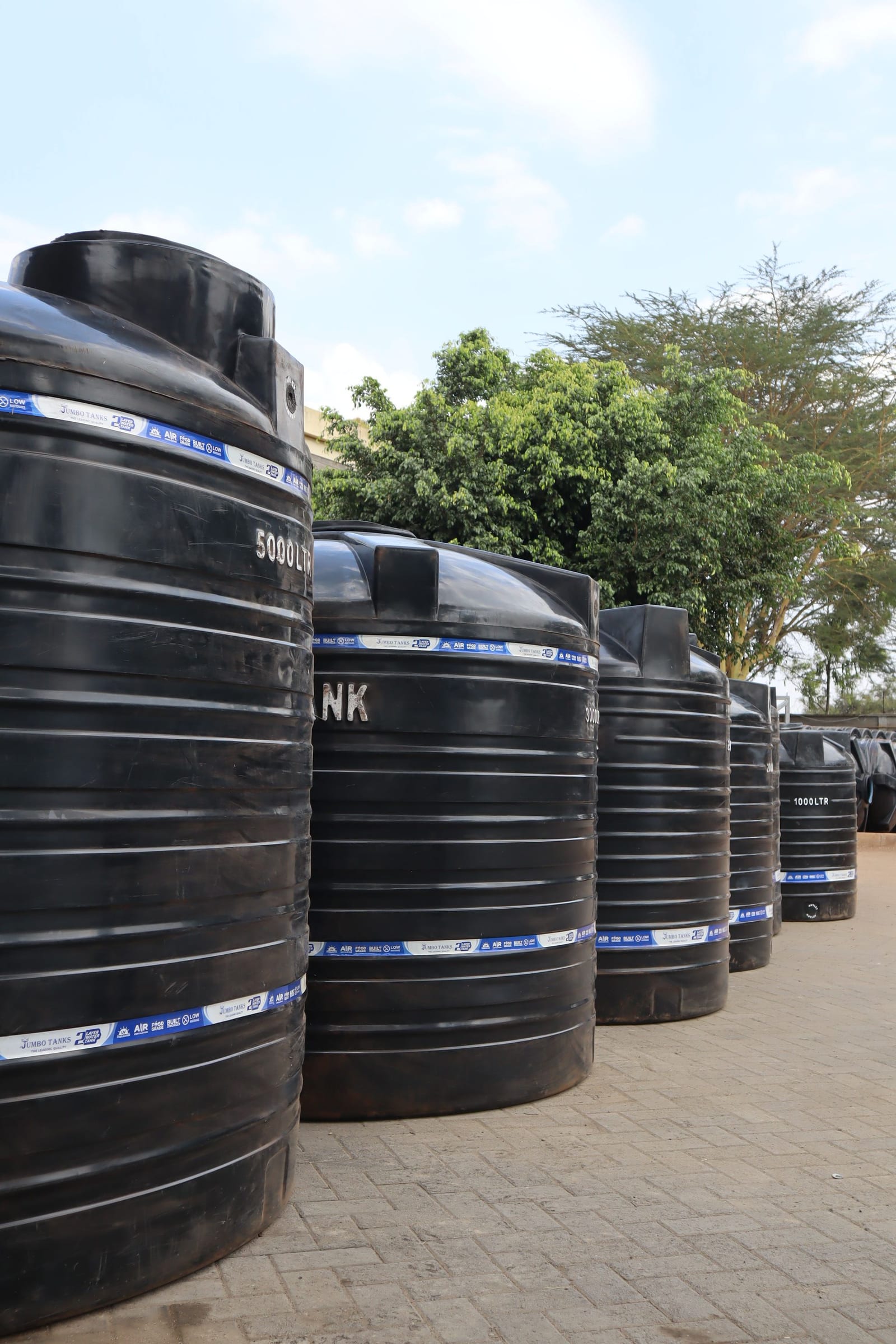Jumbo cylindrical tanks stepping down through the factory yard, from a 5,000 litre tank in the foreground to a 1,000 litre tank at the far end.